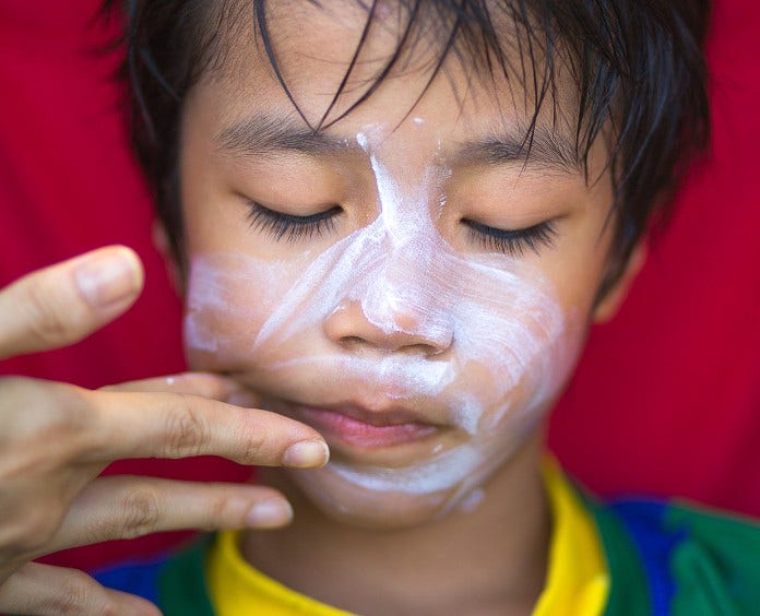 a young boy closes his eyes as someone applies sunscreen to his fact