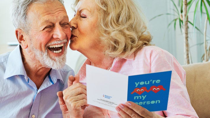 senior wife kissing husband on cheek while reading Valentine's card
