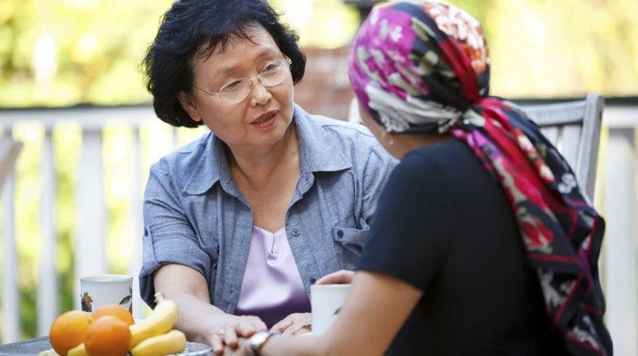 woman comforts and cancer patient in head scarf outside at table