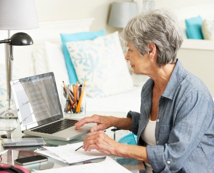 woman in home office reading a document on laptop computer
